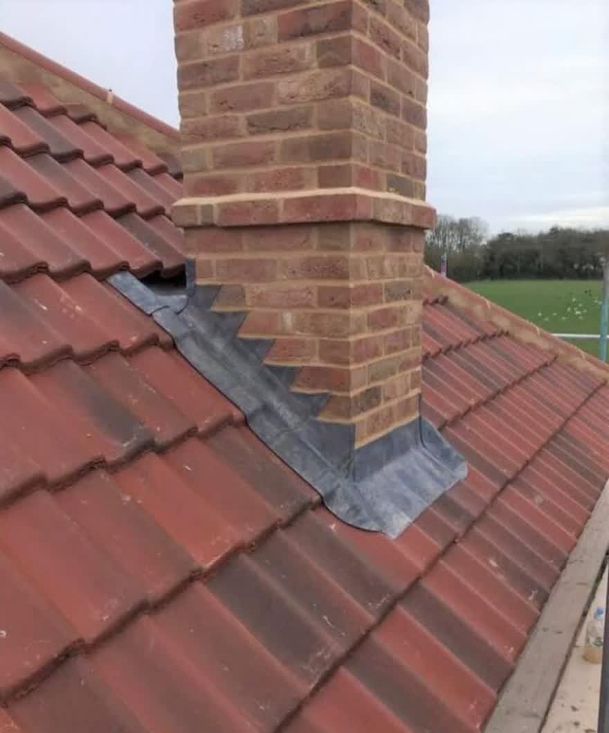 Stepped lead flashing at the base of a brick chimney on a red tiled roof