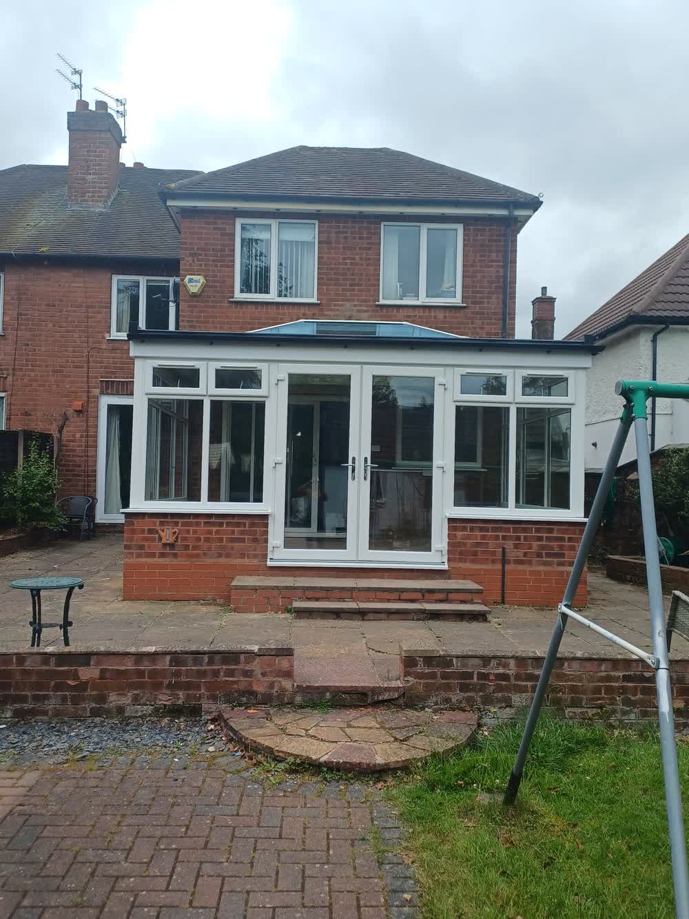 Rear of a house with a newly tiled conservatory roof and block paved patio
